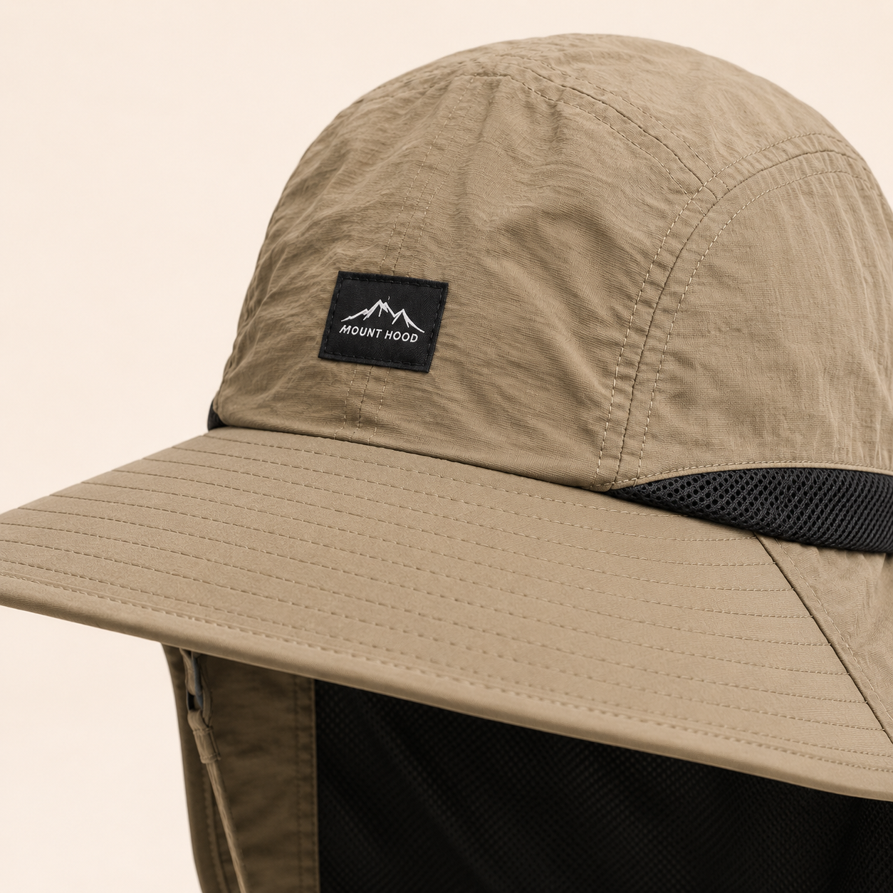 A close-up of a beige wide-brim sun hat with a built-in neck flap and black mesh chin strap, featuring a black brand patch that reads 'MOUNT ROOSE' on the front.