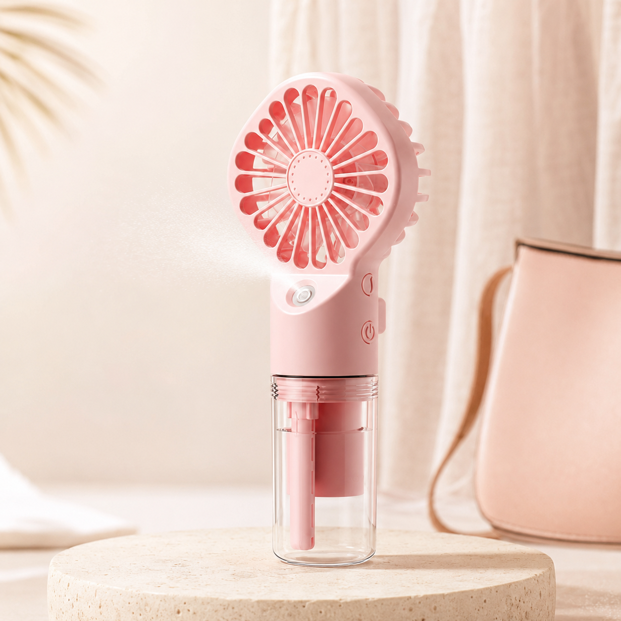 A pink portable handheld fan with a clear water reservoir, shown spraying mist on a beige pedestal with a soft pink bag in the background.
