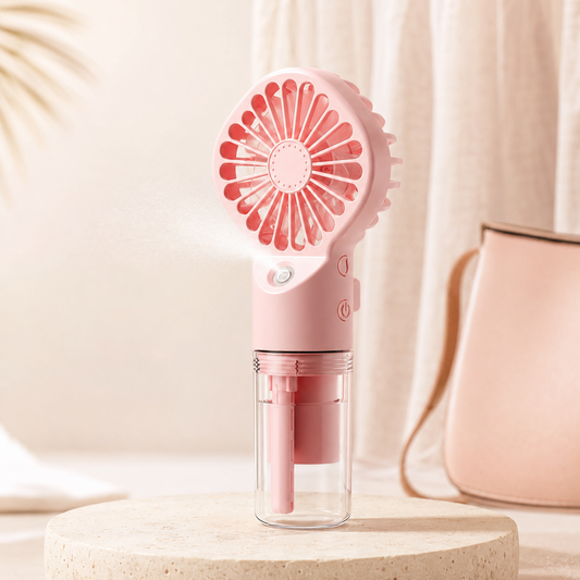 A pink portable handheld fan with a clear water reservoir, shown spraying mist on a beige pedestal with a soft pink bag in the background.