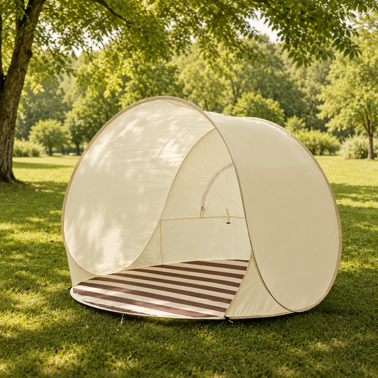 A dome-shaped pop-up canopy tent in cream with a striped floor mat, set up on a grassy lawn under a large tree in a park.
