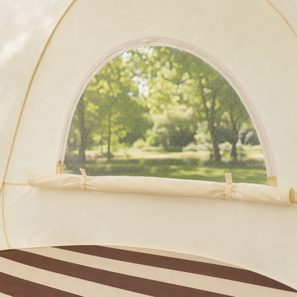 Close-up of the interior of a cream-colored dome tent, showing a mesh window with a blurred green forest background and a striped floor mat.