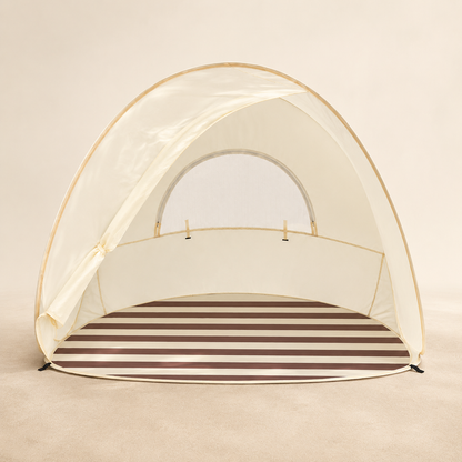 A dome-shaped beach tent with a cream-colored mesh canopy and a brown and cream horizontally striped floor, set against a solid beige background.