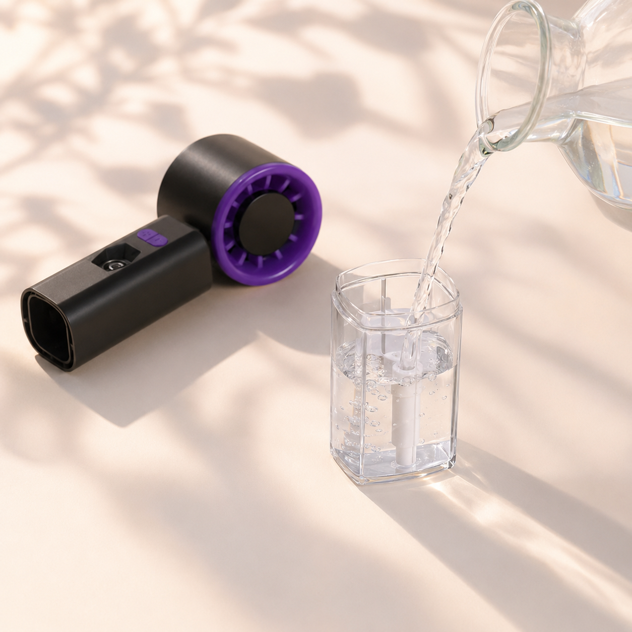 A handheld fan device in matte black with a purple circular grille is shown beside a glass being filled with water from a clear pitcher. The scene is lit by warm natural light with soft leaf shadows on a light beige surface.