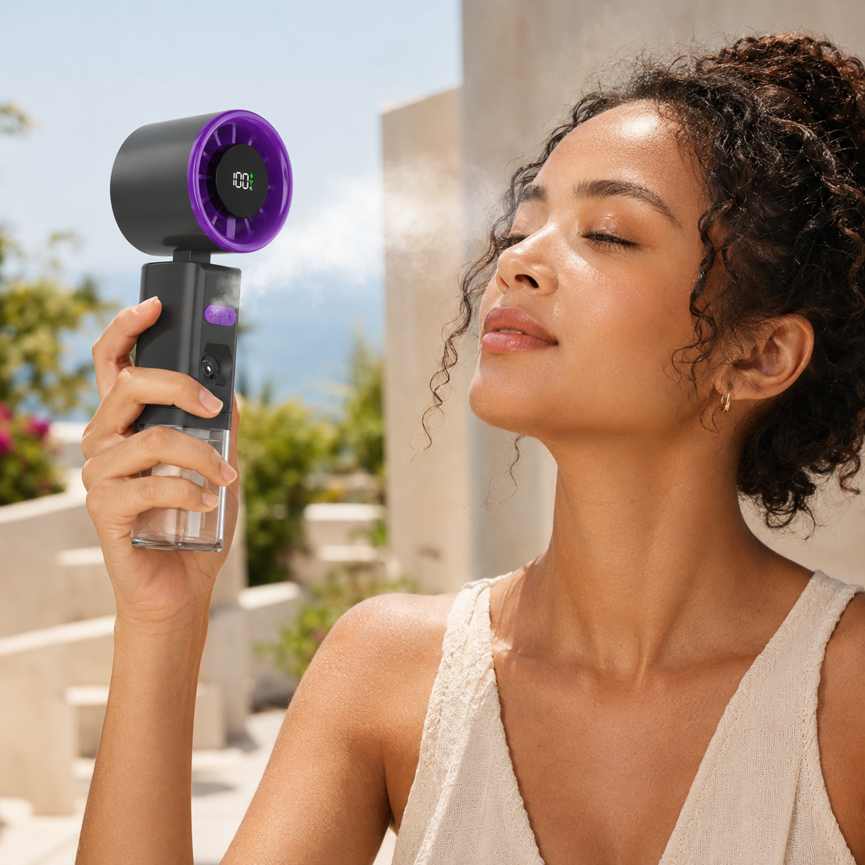 A woman outdoors holds a handheld cooling fan with a dark gray body and purple accents. The fan has a digital temperature display on the circular head.